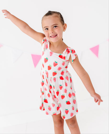 Young girl wearing a strawberry-patterned outfit on a white background with pink triangle flags.