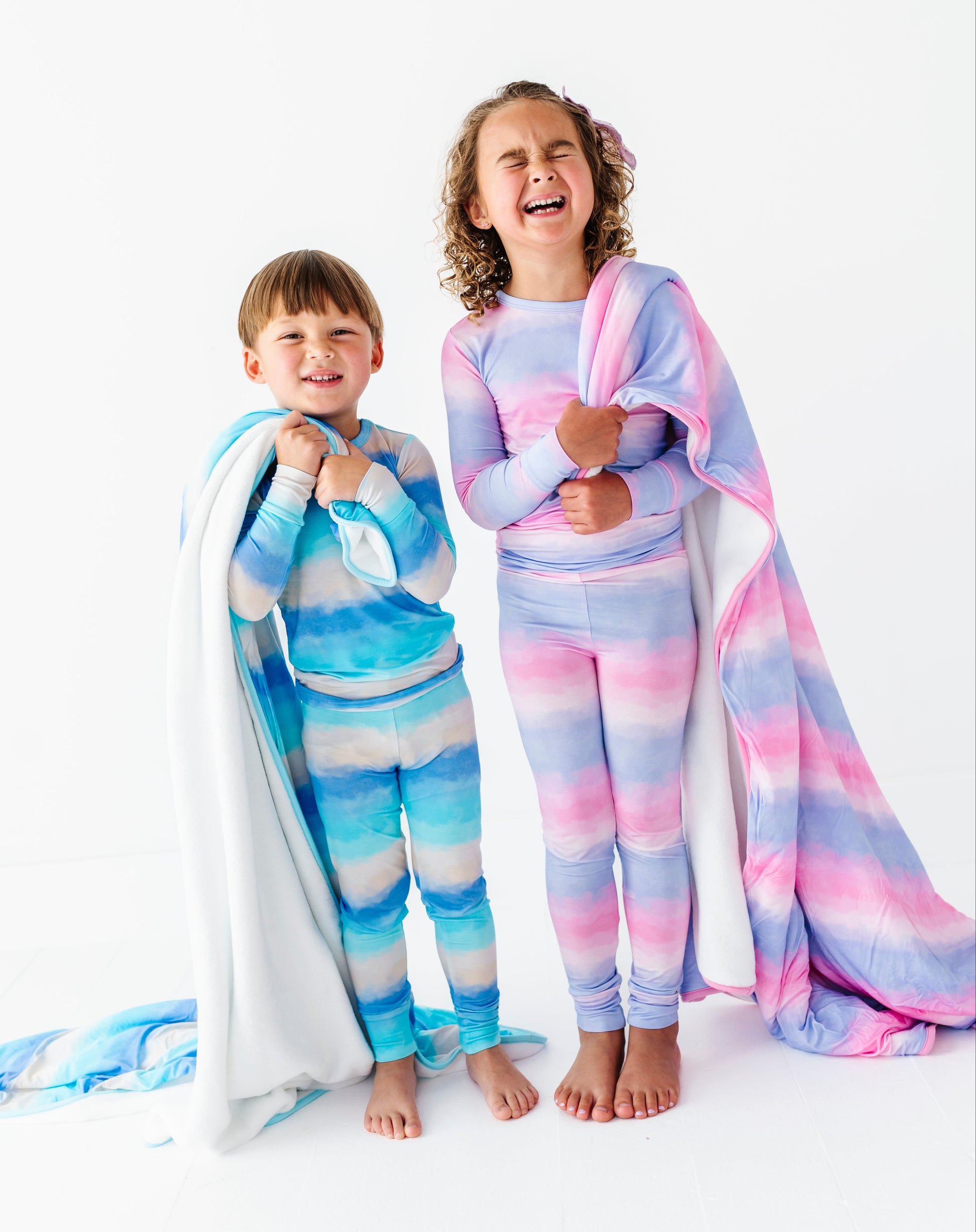 Two children wearing colorful bamboo pajamas with matching blankets on a white background
