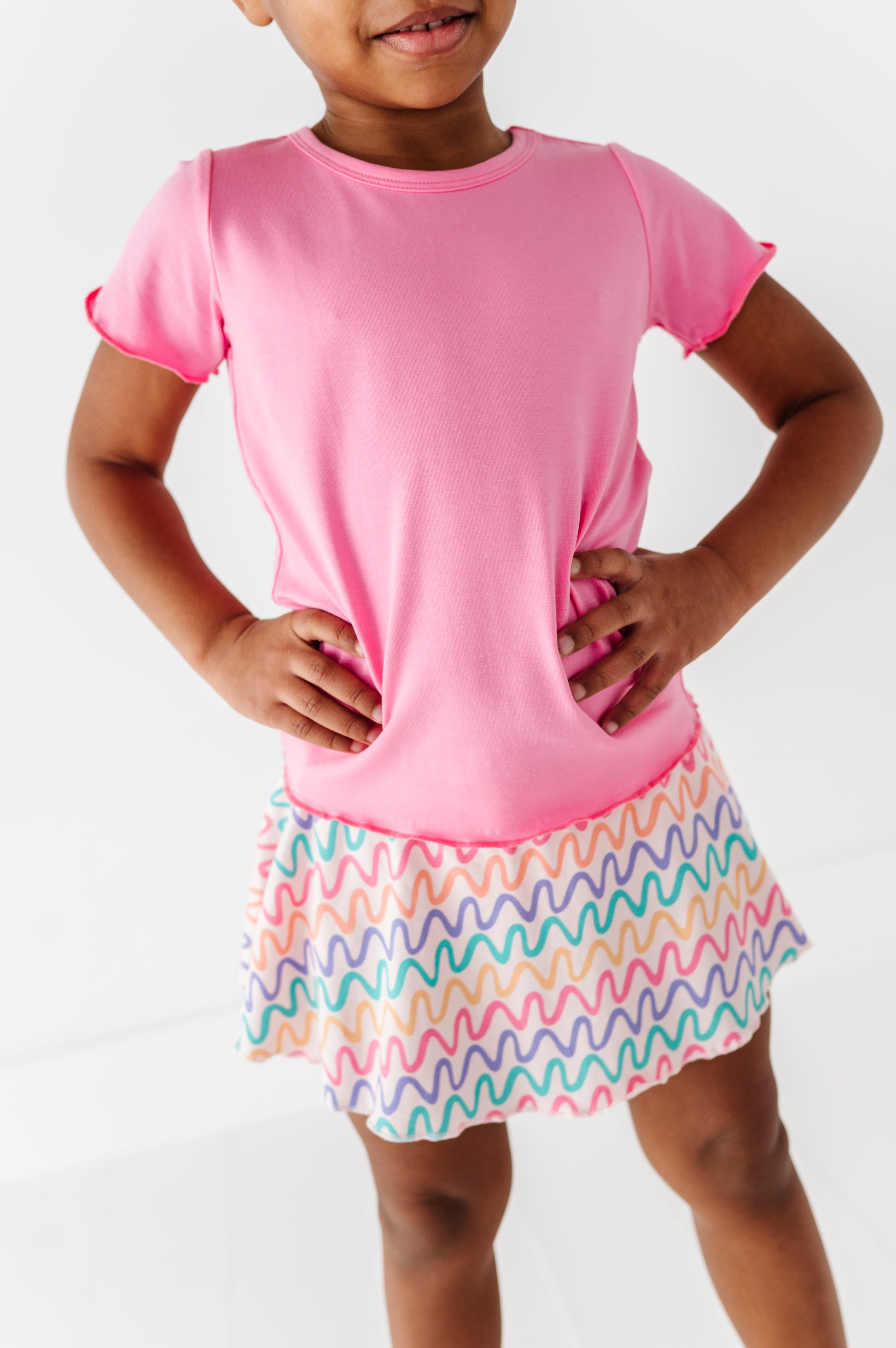 Child wearing a pink bamboo/cotton shirt and colorful bamboo skort on a white background