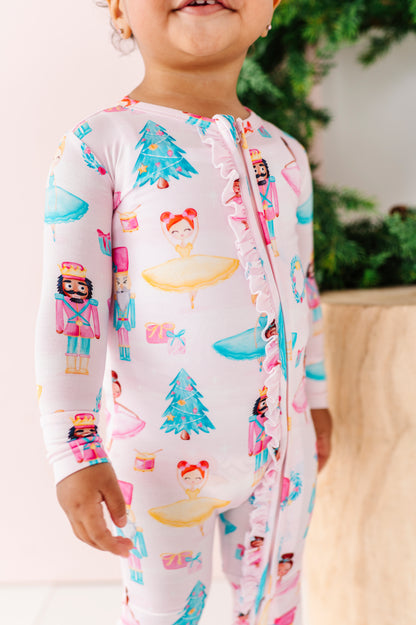 Child wearing light pink pajamas with ballerinas, nutcrackers, Christmas trees, and presents.