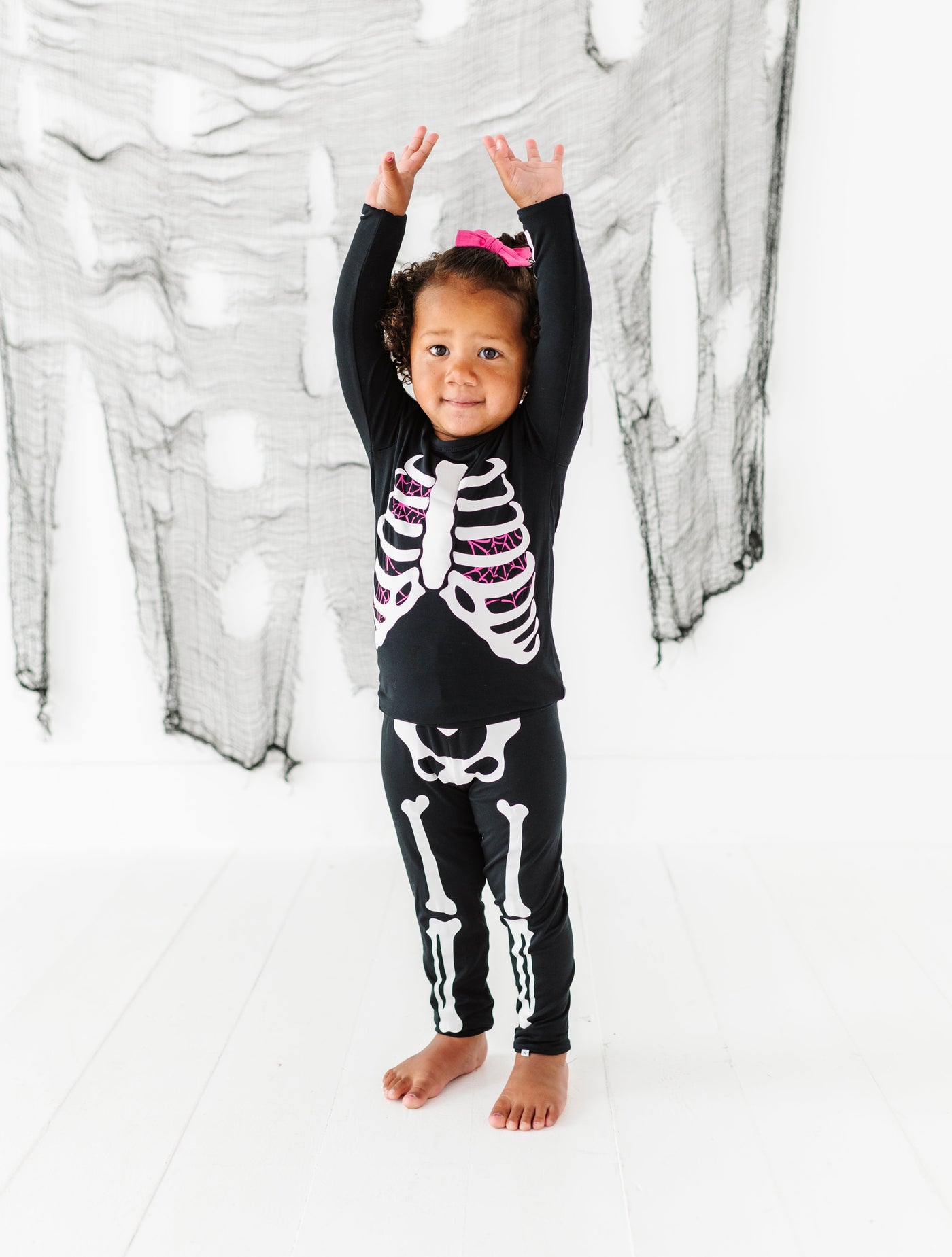 Child wearing a skeleton-themed outfit in front of a white curtain with black patterns.
