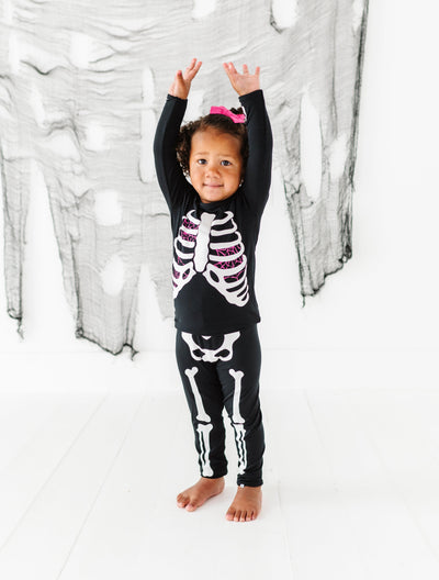 Child wearing a skeleton-themed outfit in front of a white curtain with black patterns.