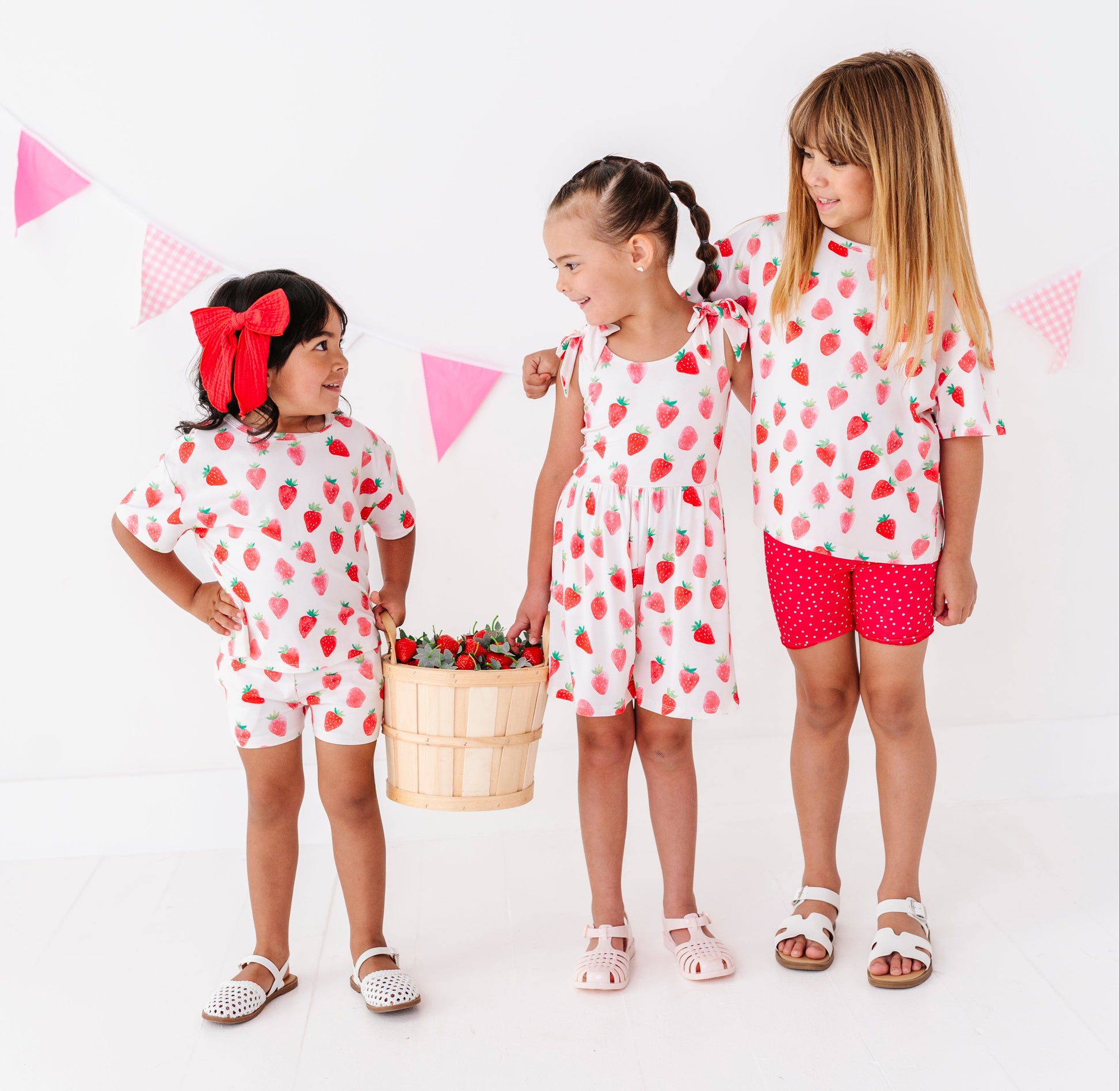 Three children wearing matching outfits with red and white patterns on a white background.