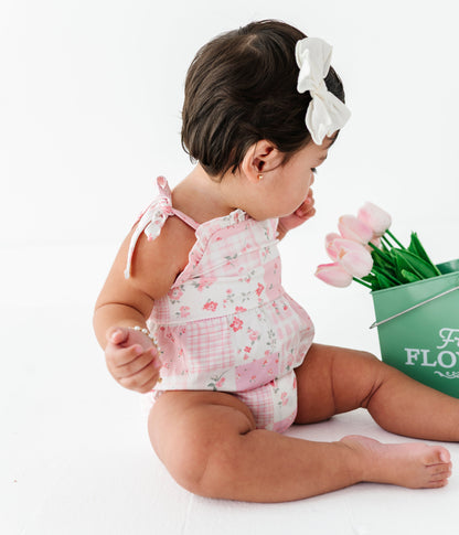 Baby girl in a floral bamboo outfit holding pink tulips next to a green bucket with flowers on a white background