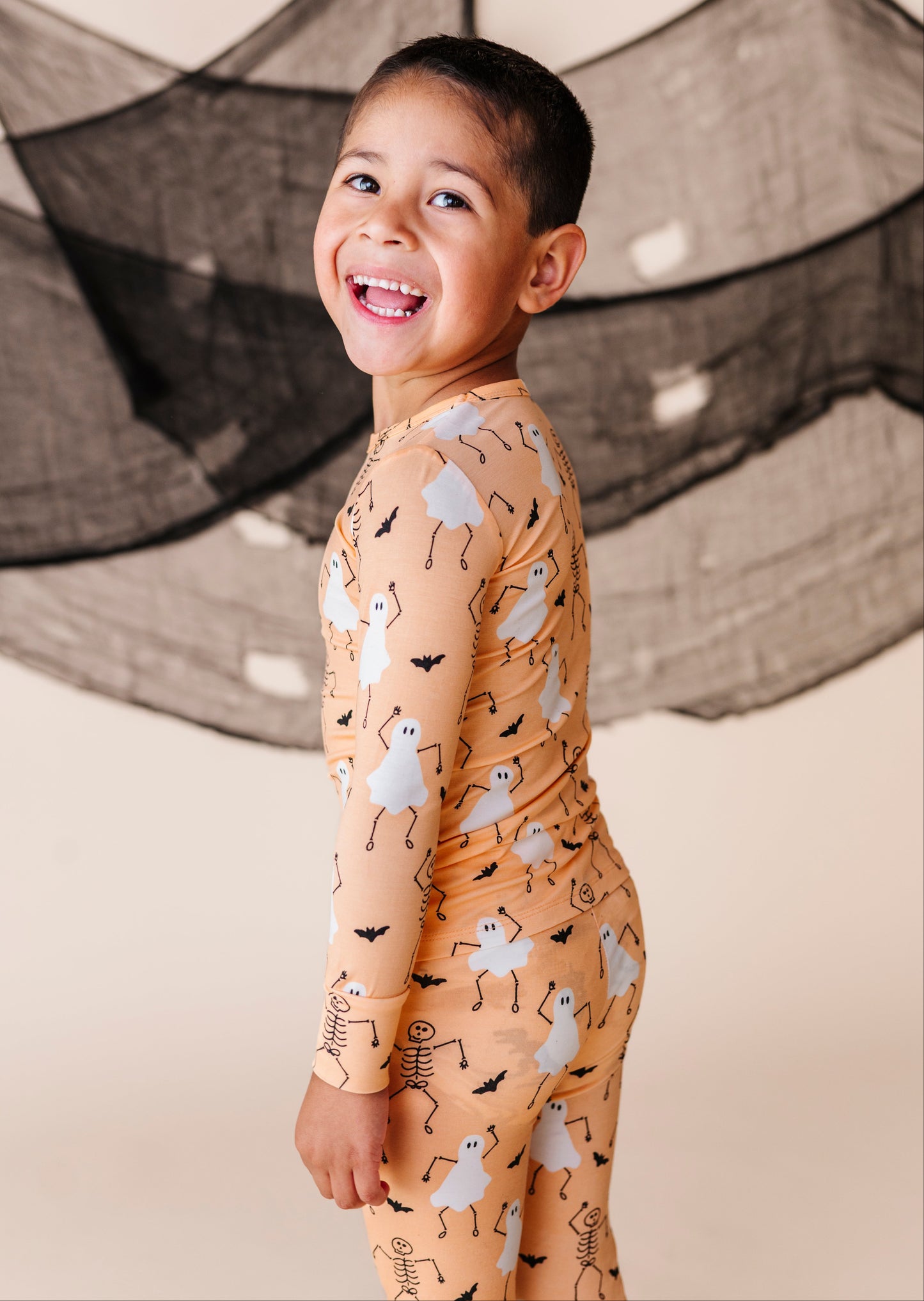 Child wearing a Halloween-themed PAJAMA SET with ghosts and skeletons against a neutral background