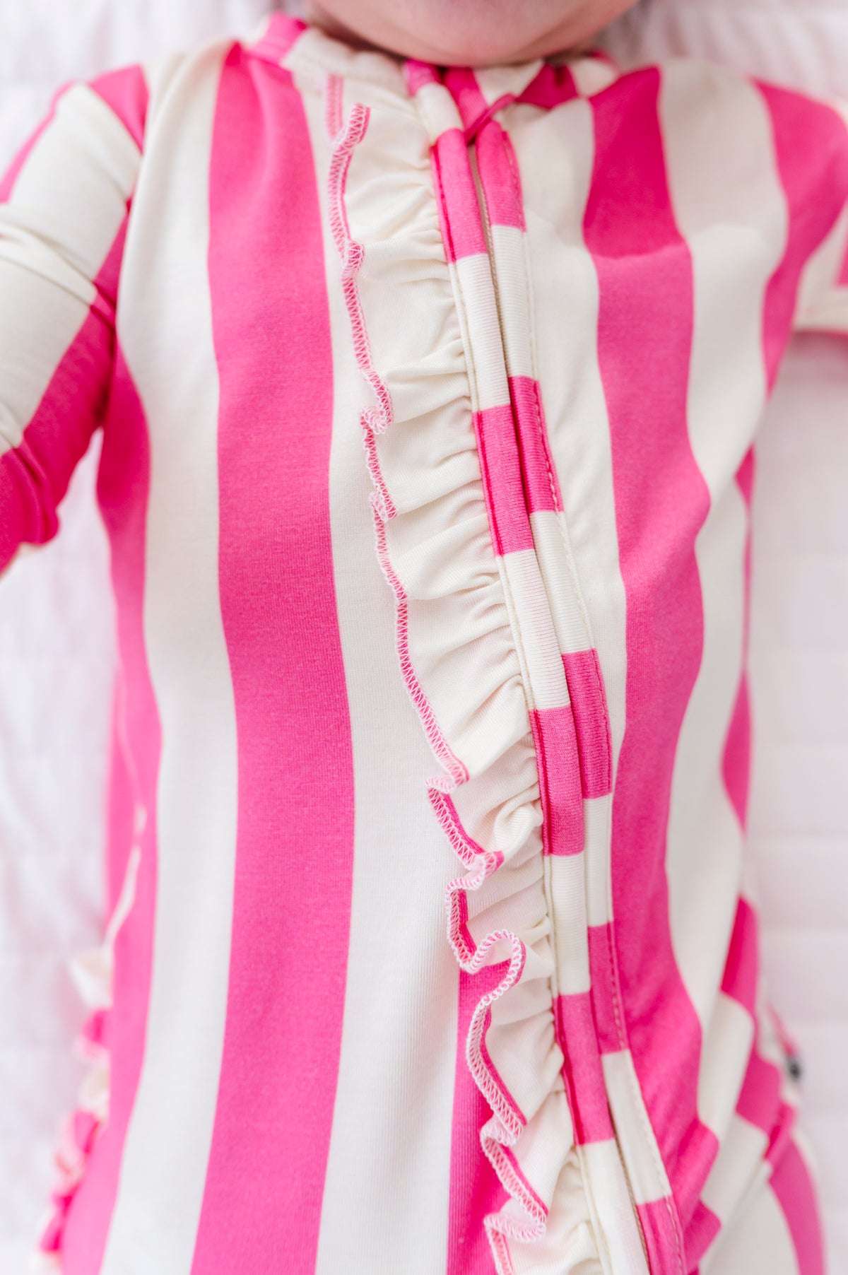A close-up of a baby's torso wearing a pink and cream striped long-sleeve sleeper with a ruffle trim down the front.
