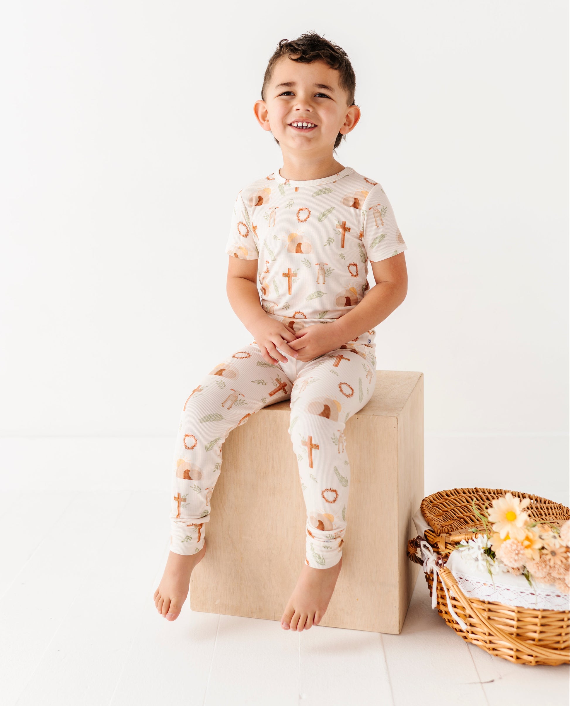Child wearing a patterned outfit sitting on a block with a basket of flowers in the background