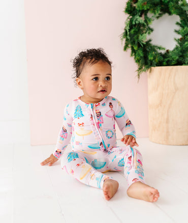Baby in a Christmas bamboo zip romper sitting on a white surface with a decorative wreath in the background.
