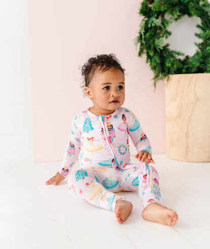 Baby in a Christmas bamboo zip romper sitting on a white surface with a decorative wreath in the background.
