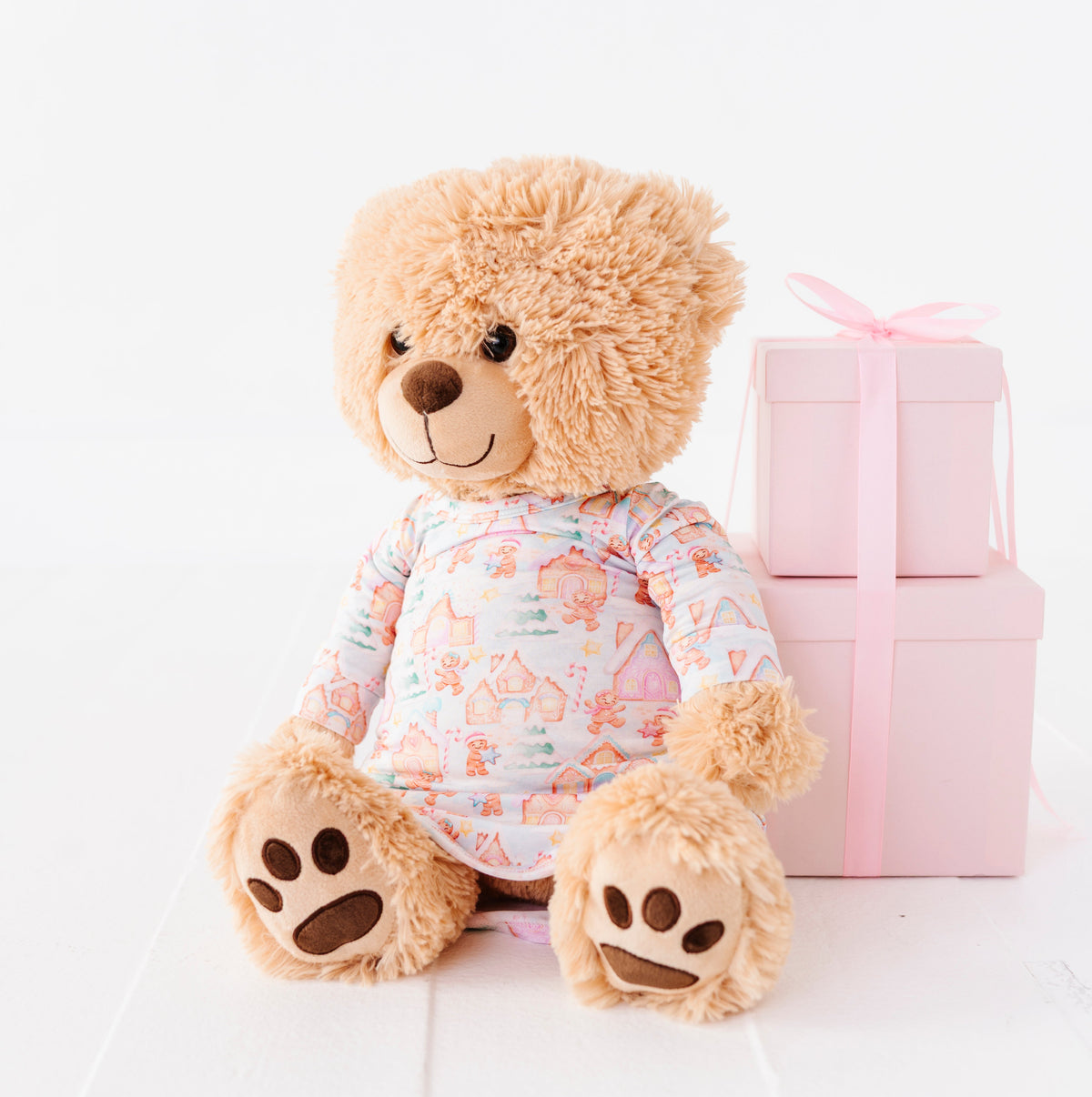 A 18" teddy bears resting against a pile of pink presents wearing a Christmas gingerbread village-themed bamboo gown