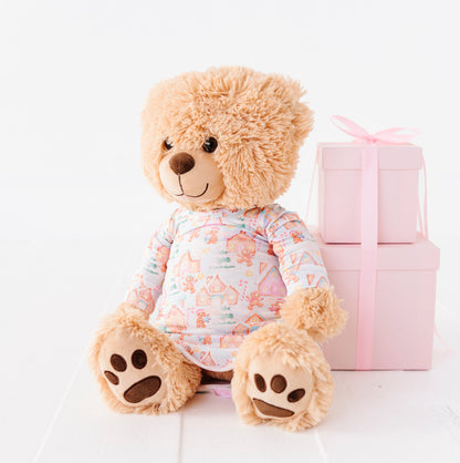 A 18" teddy bears resting against a pile of pink presents wearing a Christmas gingerbread village-themed bamboo gown
