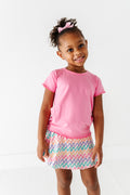 Young girl wearing a pink bamboo/cotton shirt and colorful bamboo skort on a white background