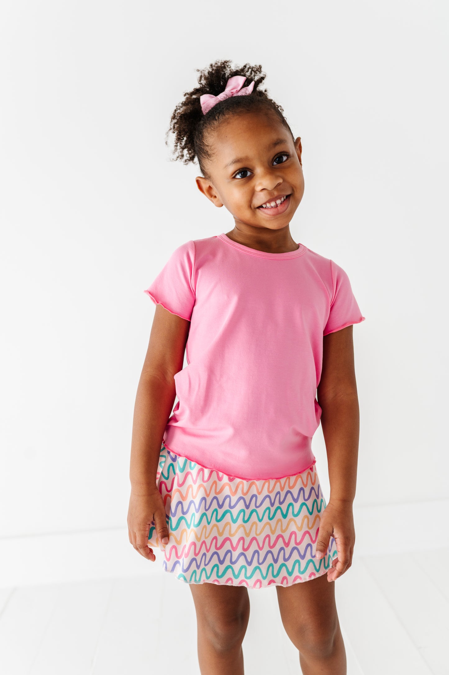 Young girl wearing a pink bamboo/cotton shirt and colorful bamboo skort on a white background