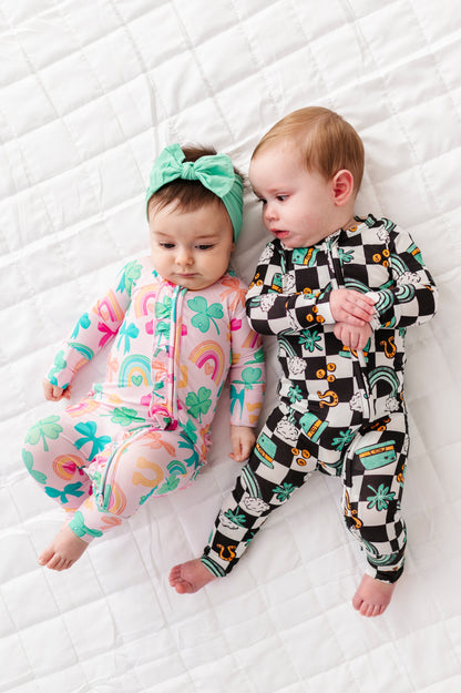 Two babies wearing colorful St. Patrick's Day themed bamboo onesies lying on a white textured blanket