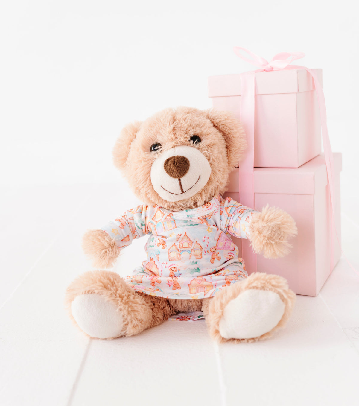 A 13" teddy bears resting against a pile of pink presents wearing a Christmas gingerbread village-themed bamboo gown