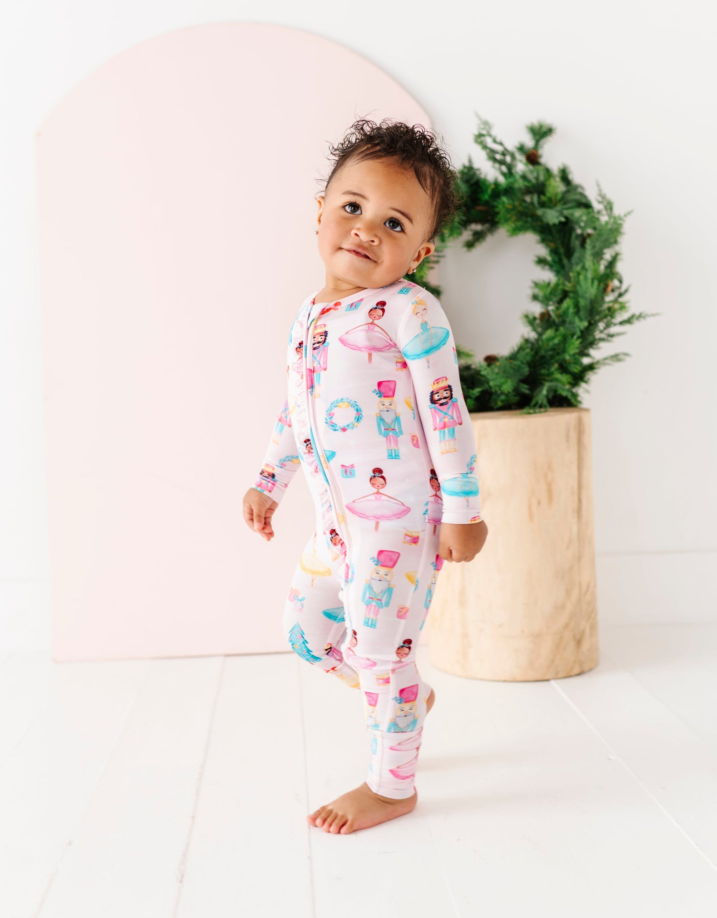 Child wearing a bamboo convertible romper with nutcrackers, ballerinas, presents, wreaths, and Christmas trees