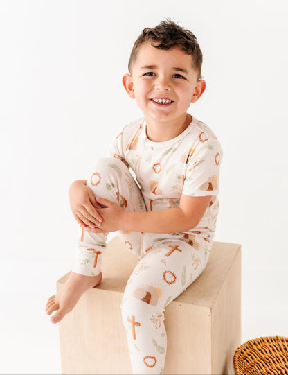 Child wearing a white onesie with a cross print, sitting on a light-colored block.