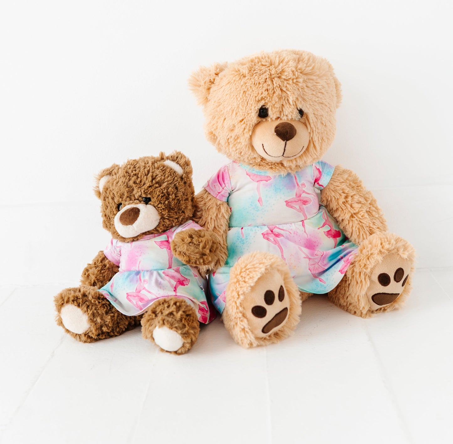 Two teddy bears wearing colorful bamboo dresses sitting on a white background