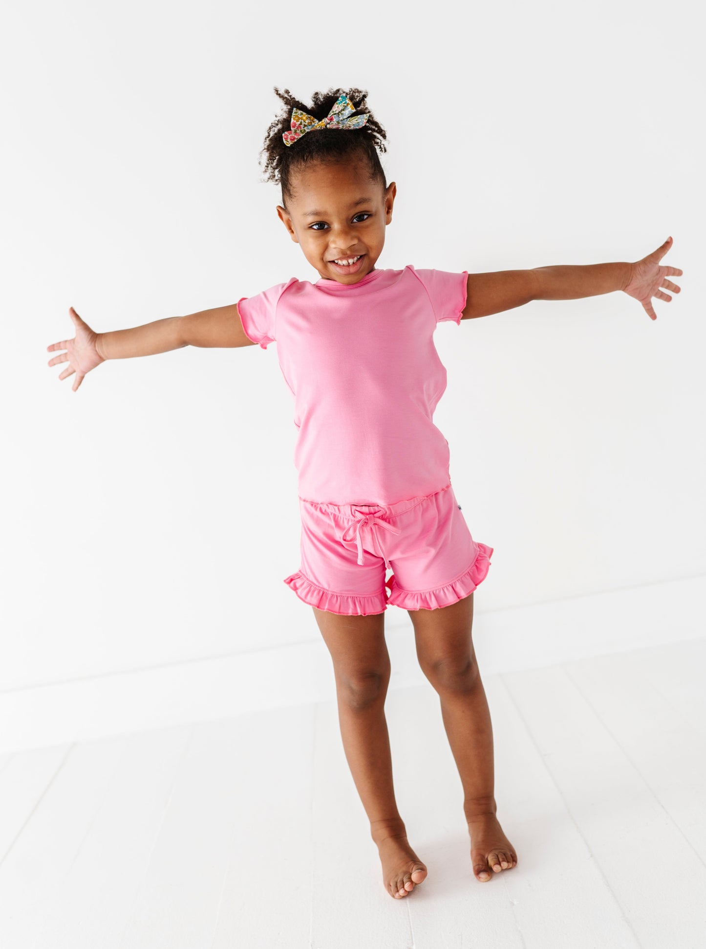 Young girl in a pink bamboo/cotton outfit with arms outstretched on a white background