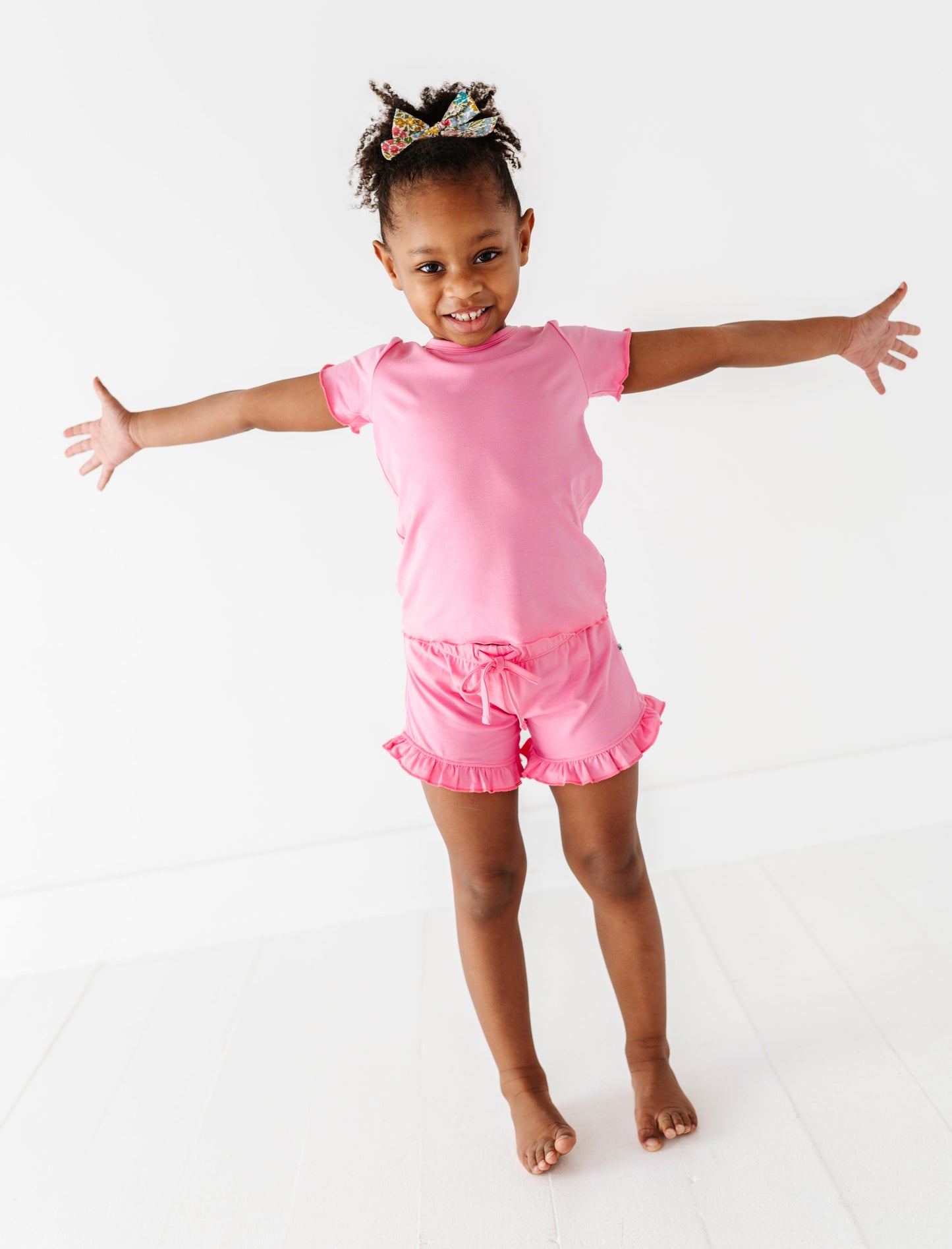 Young girl in a pink bamboo/cotton outfit with arms outstretched on a white background