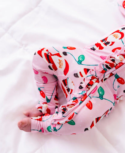 A close-up detail shot of a baby girl wearing a pink ruffle bamboo convertible romper featuring  variety of Santas hanging from multicolor Christmas lights 