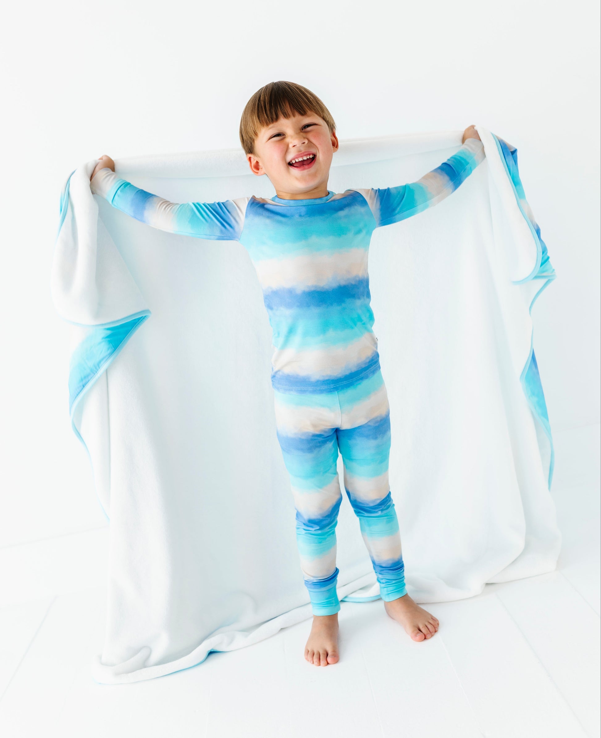 Child wearing a blue and white striped bamboo pajama set holding a matching blanket.