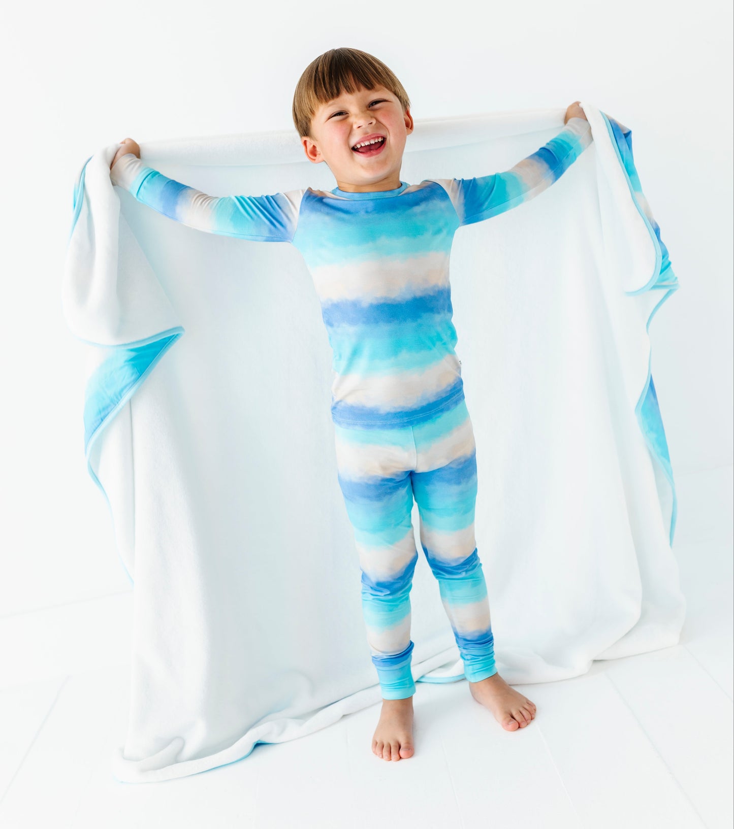 Child wearing a blue and white striped bamboo pj set holding a matching blanket.