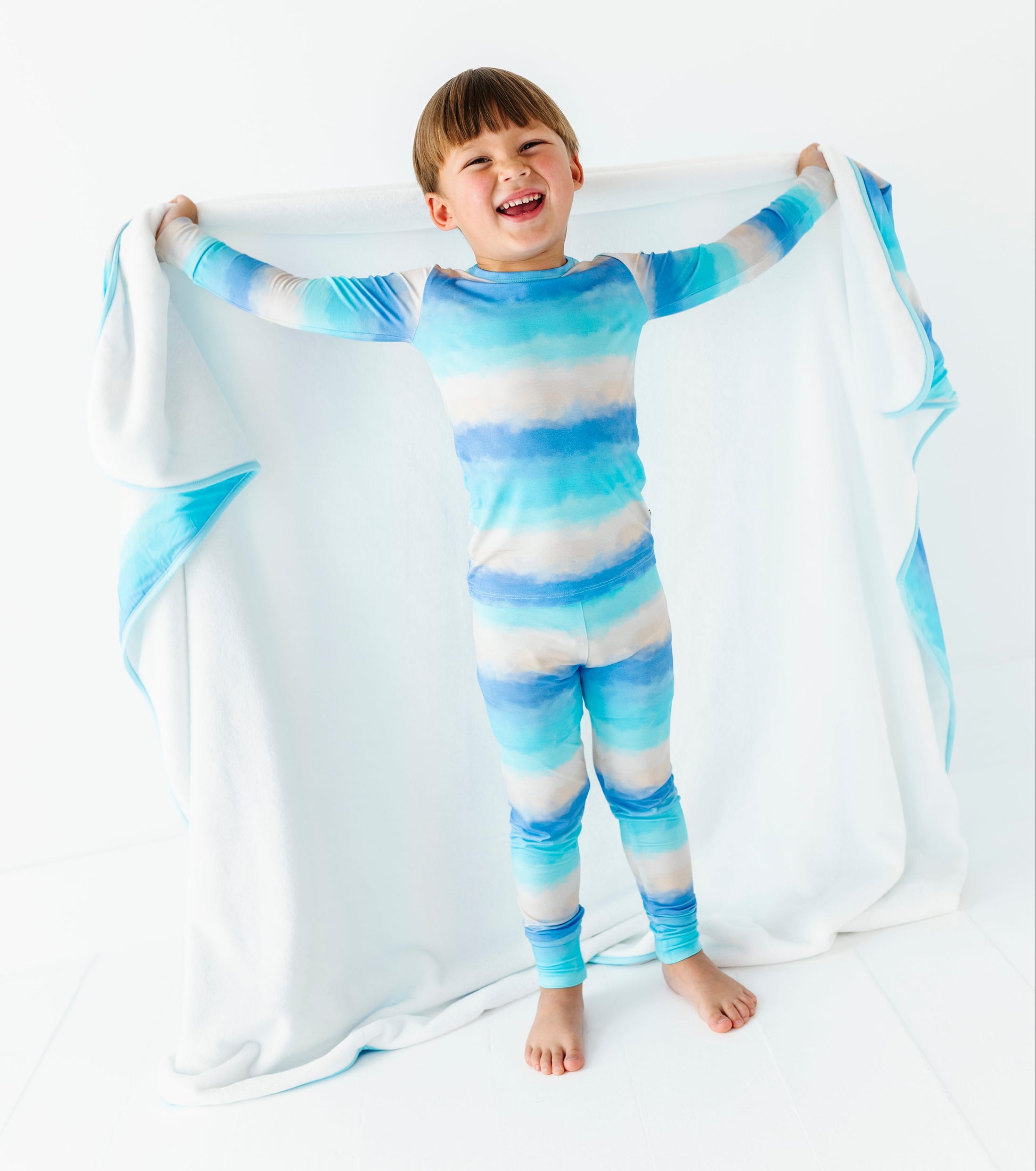Child wearing a blue and white striped bamboo pj set holding a matching blanket.