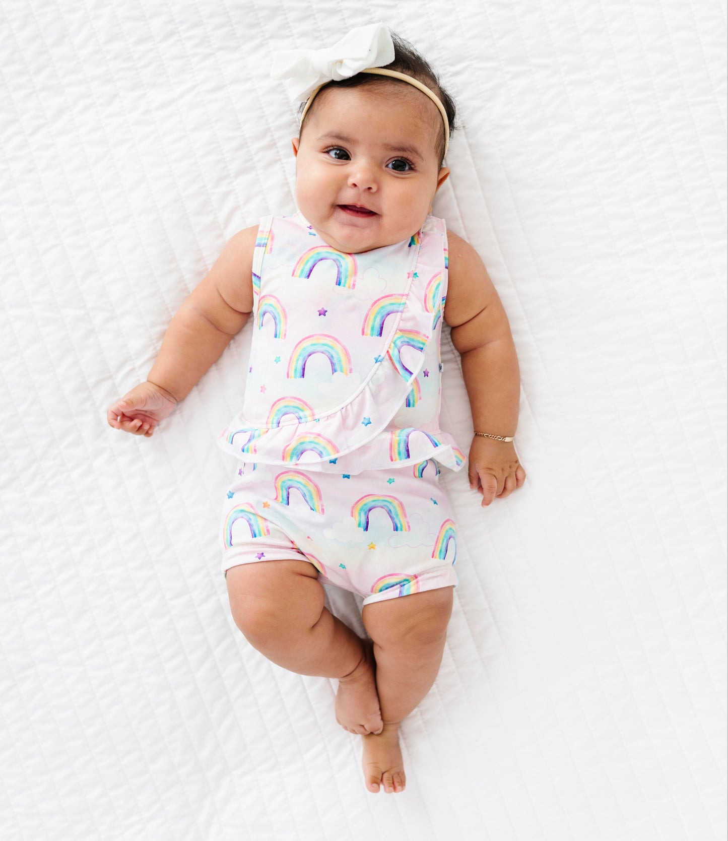 Baby wearing a bamboo cotton peplum top and bloomers set with watercolor rainbow patterns on a white blanket