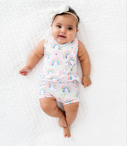 Baby wearing a bamboo cotton peplum top and bloomers set with watercolor rainbow patterns on a white blanket
