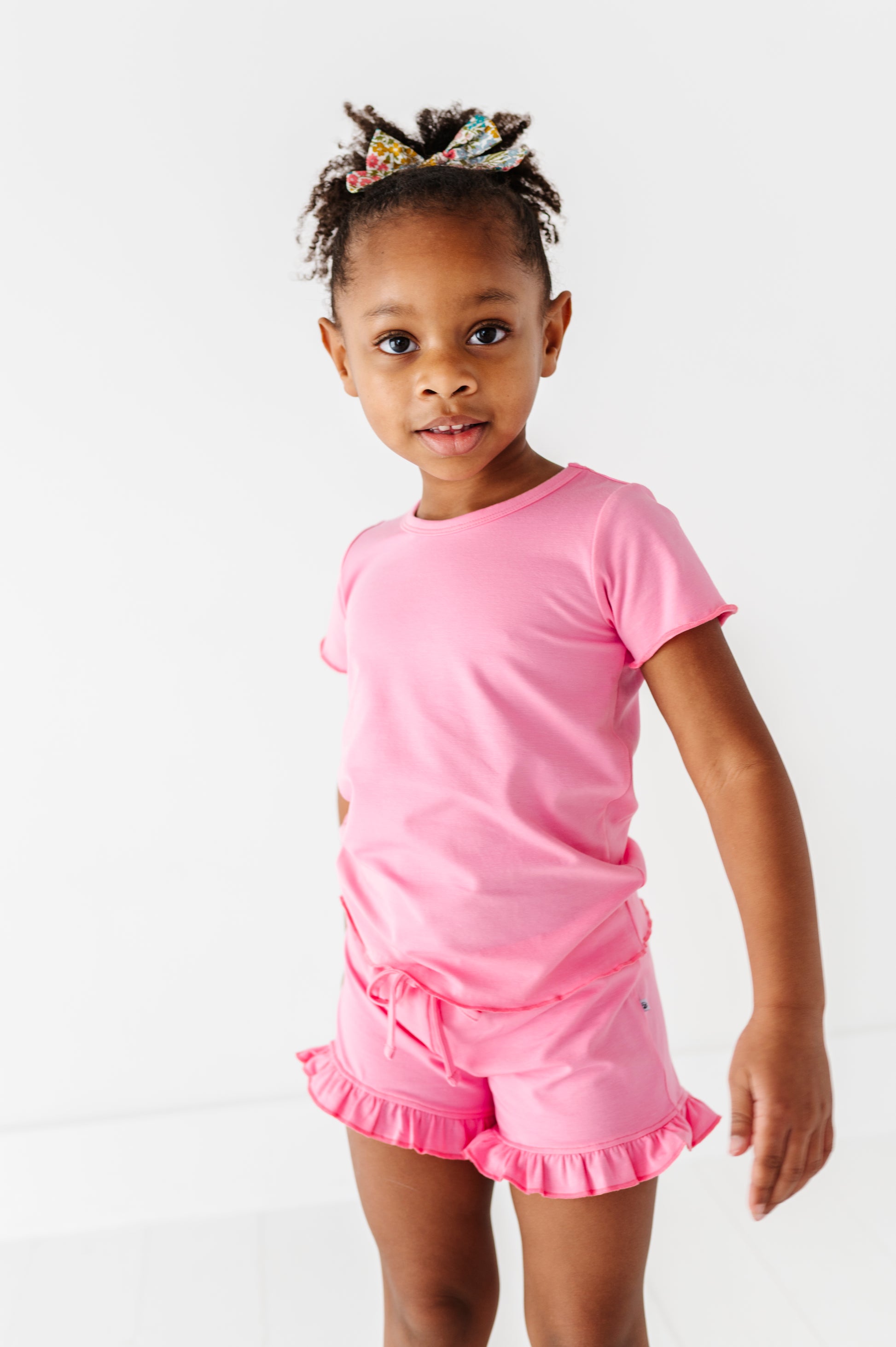 Young girl wearing a pink outfit with ruffled bamboo/cotton shorts on a white background