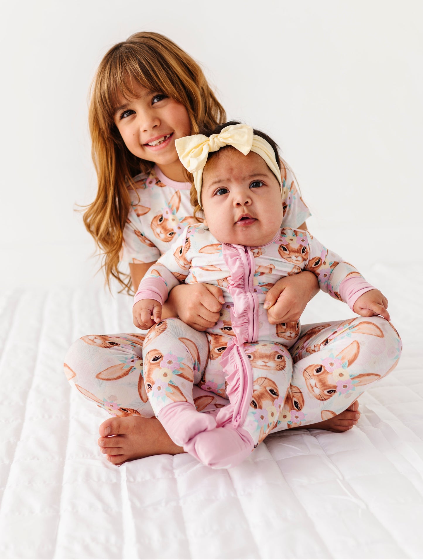 Two children in matching Easter pajamas sitting on a white blanket.
