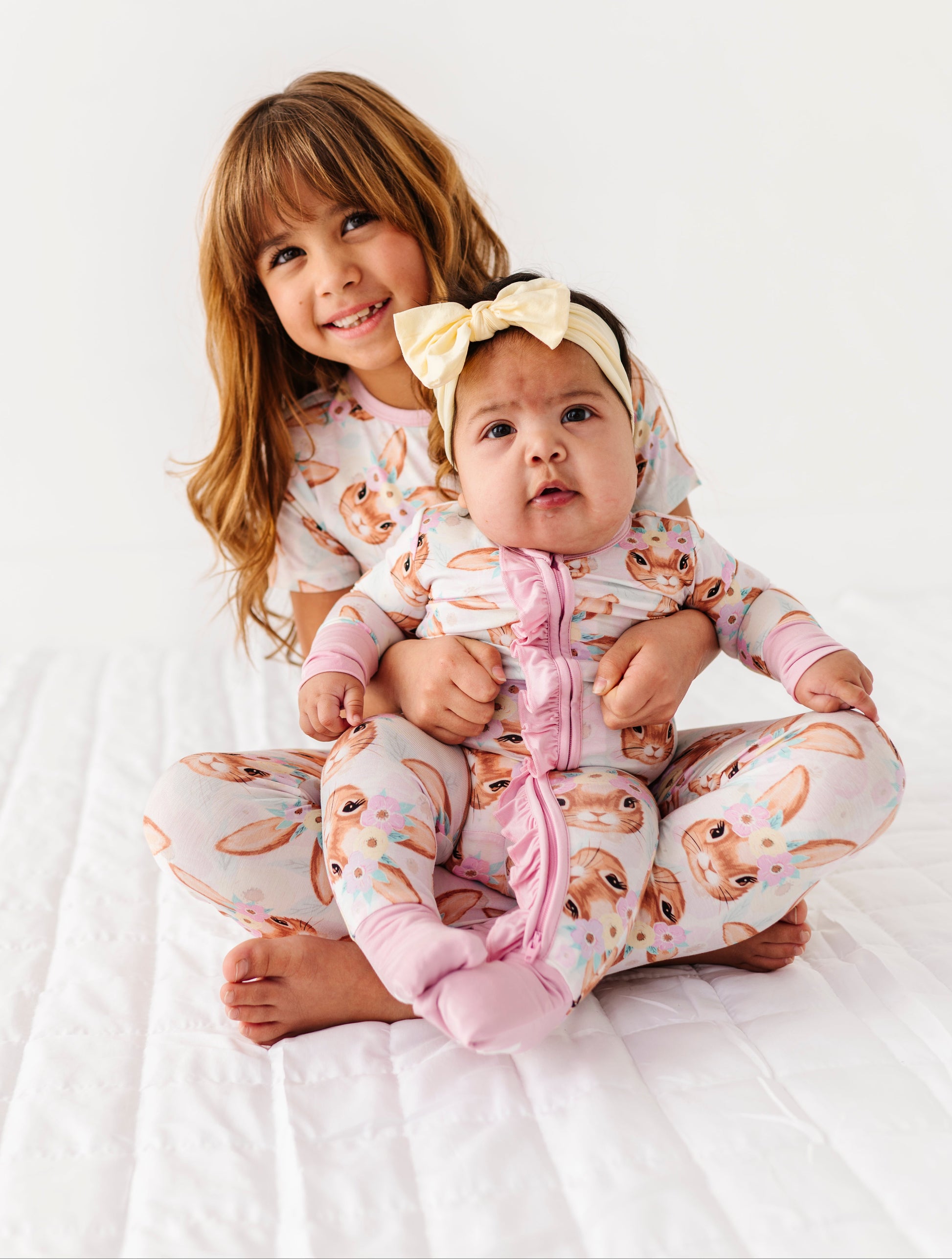 Two children in matching Easter pajamas sitting on a white blanket.