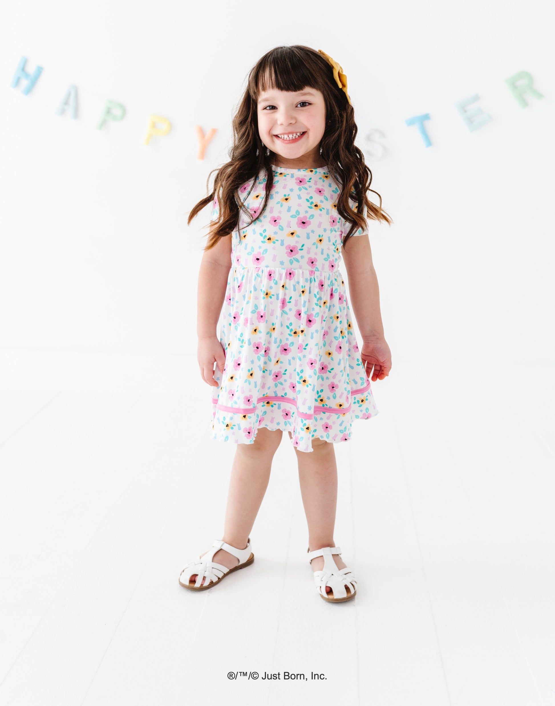 Young girl wearing a floral PEEPS® dress with 'Happy Easter' banner in the background