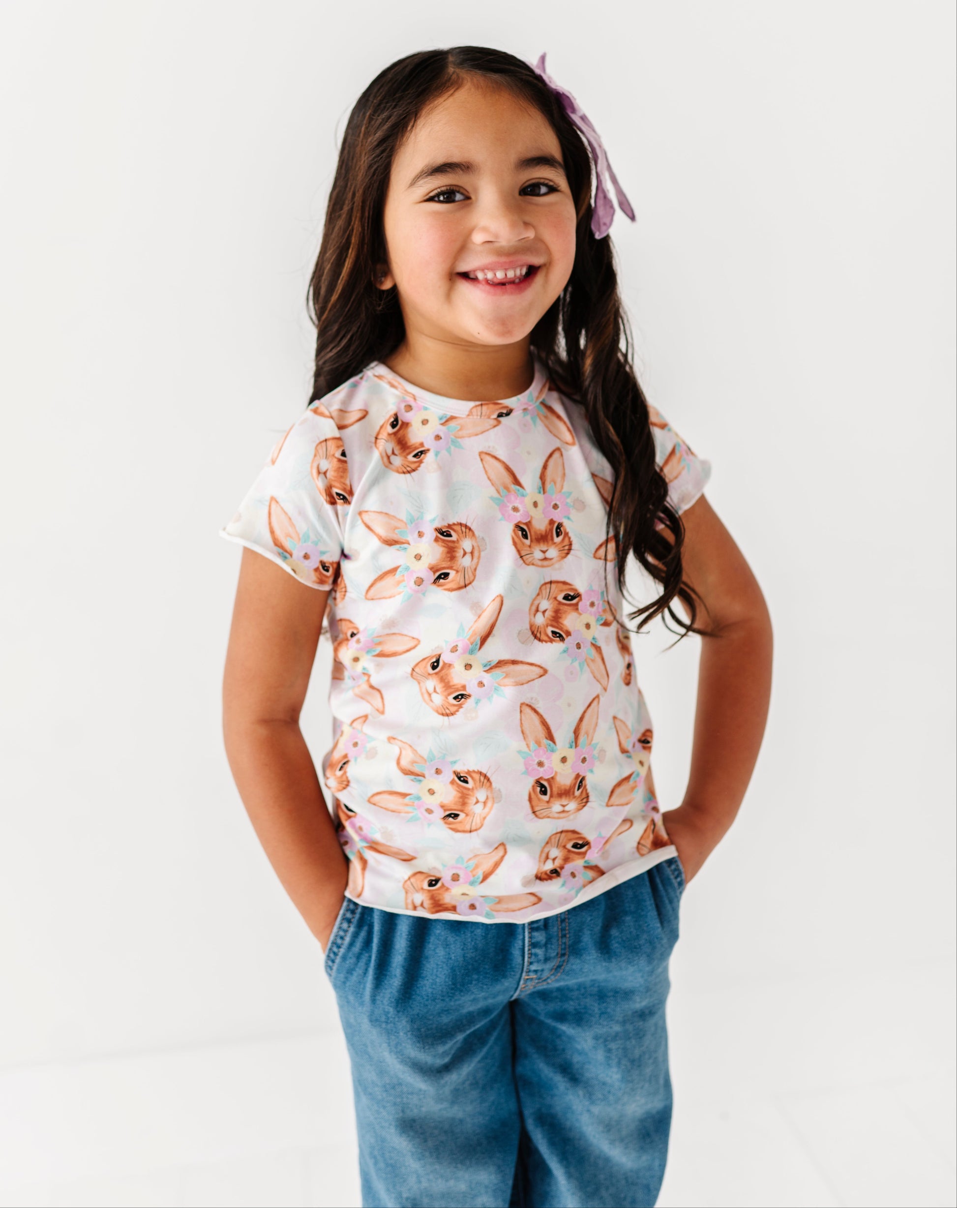 Young girl wearing a white t-shirt with bunny print and blue jeans on a white background