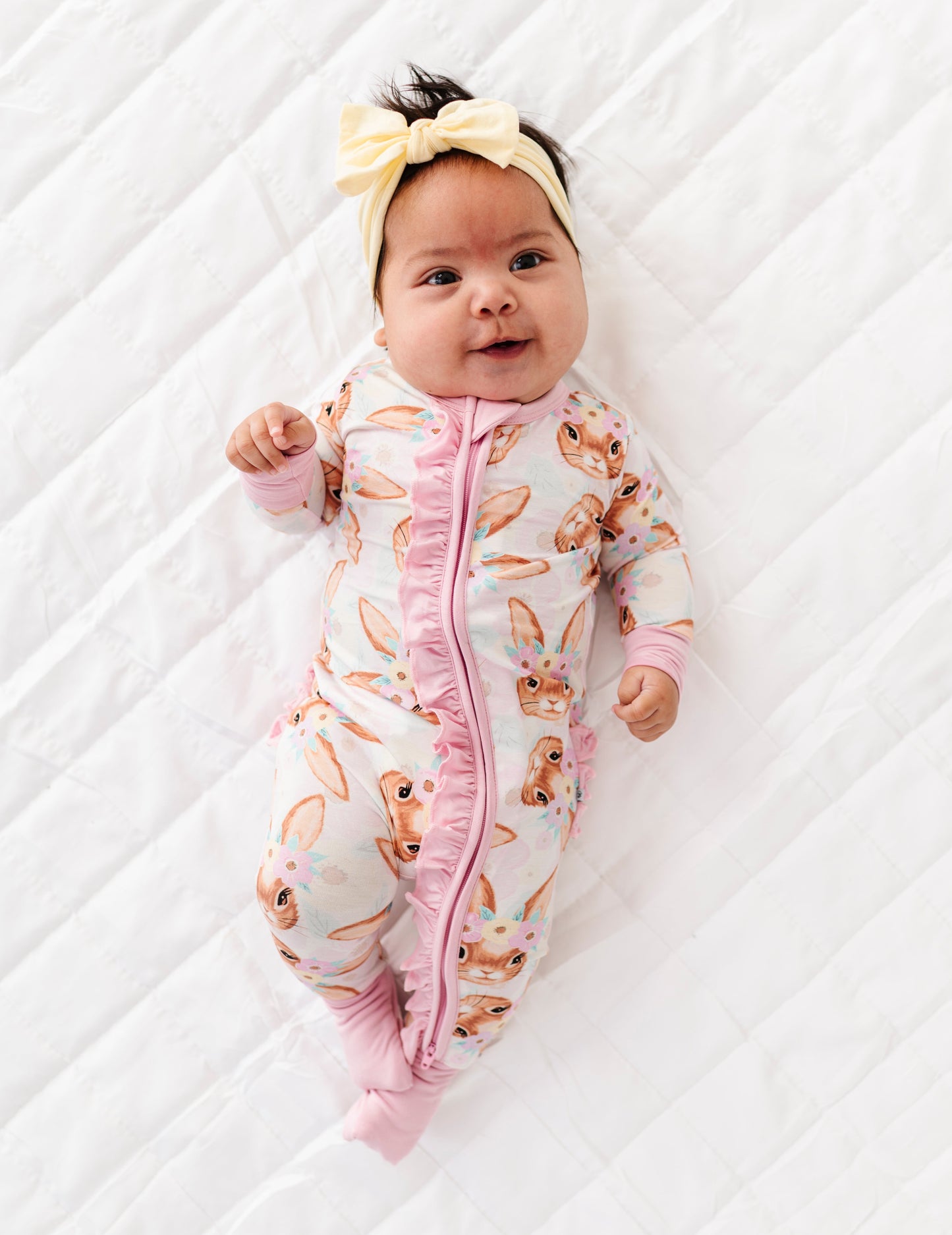 Baby in a pink bunny-patterned Easter onesie lying on a white surface