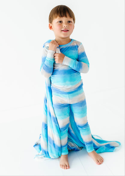 Child wearing a blue and white striped bamboo pajama set and holding a matching bamboo blanket on a white background