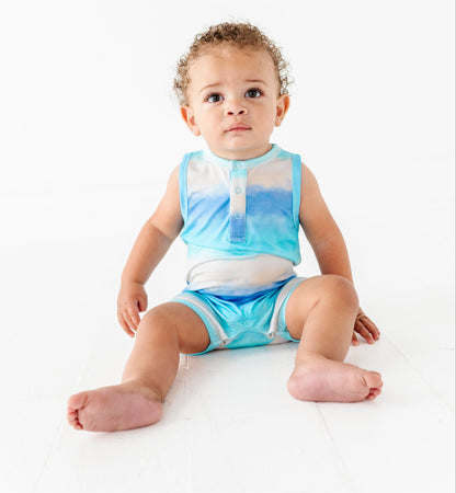 Baby sitting on a white surface wearing a blue and white sleeveless bamboo romper and diaper.
