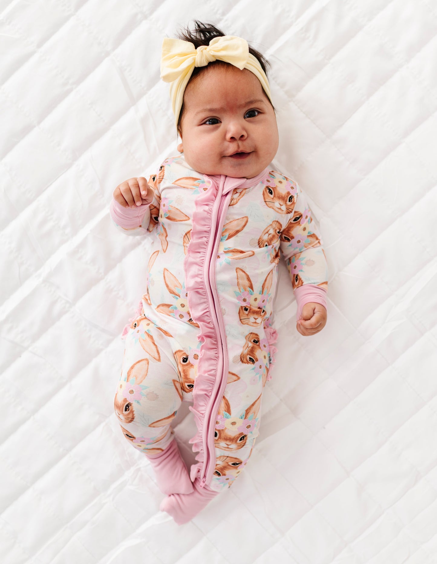 Baby in a pink bunny-patterned onesie lying on a white textured surface