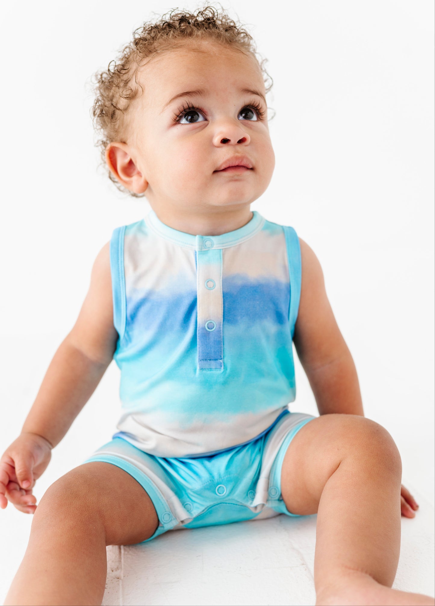 Baby wearing a blue and white gradient bamboo romper sitting on a white surface.