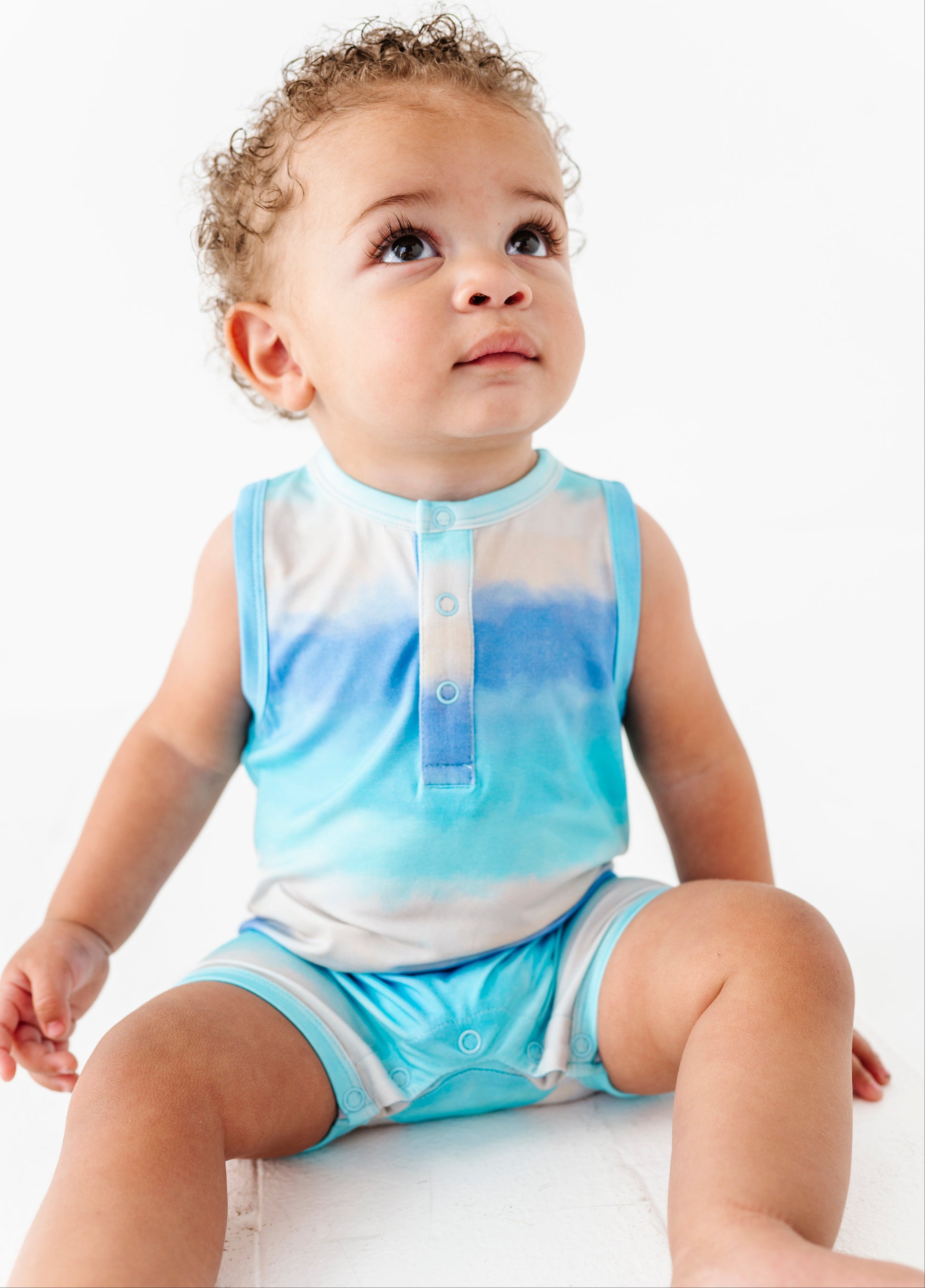 Baby wearing a blue and white gradient bamboo romper sitting on a white surface.