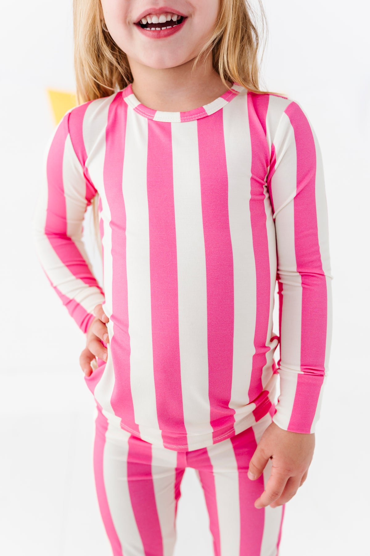 A young girl wearing a pink and white vertically striped long-sleeve top and matching striped pants, shown from the mouth down against a clean white background.