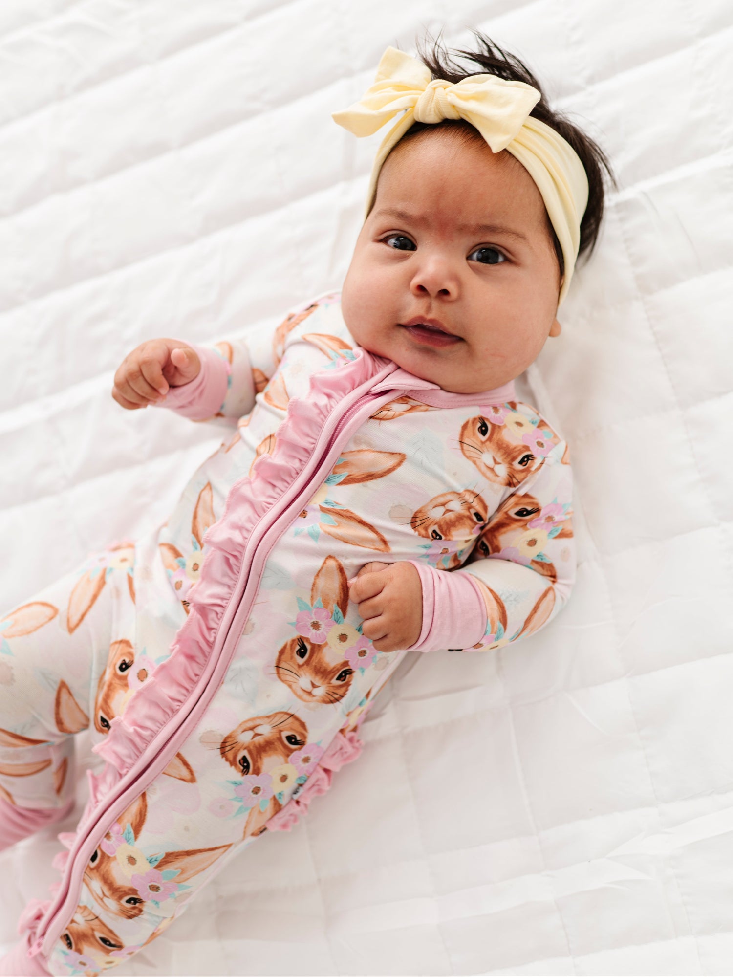 Baby wearing an Easter patterned bamboo romper with pink accents on a white textured surface