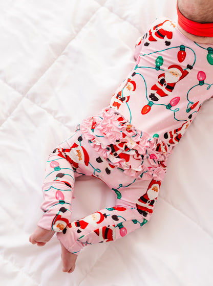 A close-up detail shot of a baby girl wearing a pink ruffle bamboo convertible romper featuring  variety of Santas hanging from multicolor Christmas lights 