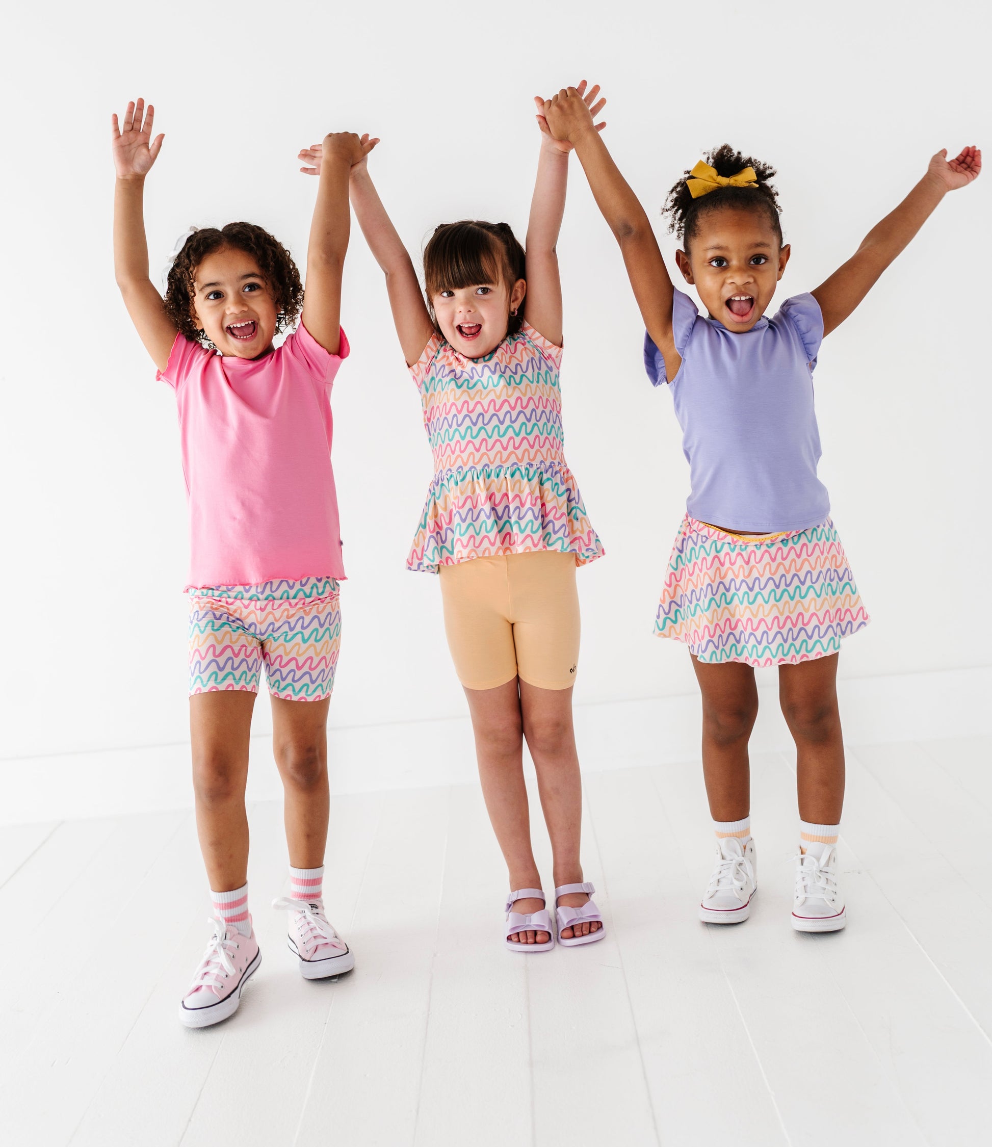 Three children in colorful outfits with arms raised on a white background