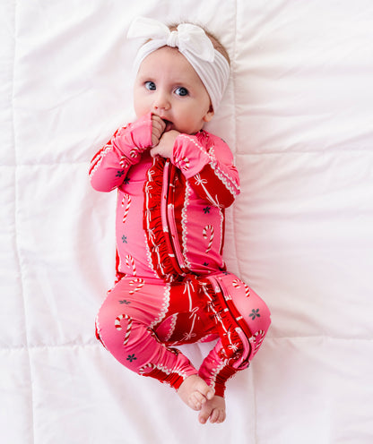 A baby girl wearing a red-and-pink bamboo Christmas convertible romper featuring ruffle detailing and foldover cuffs 