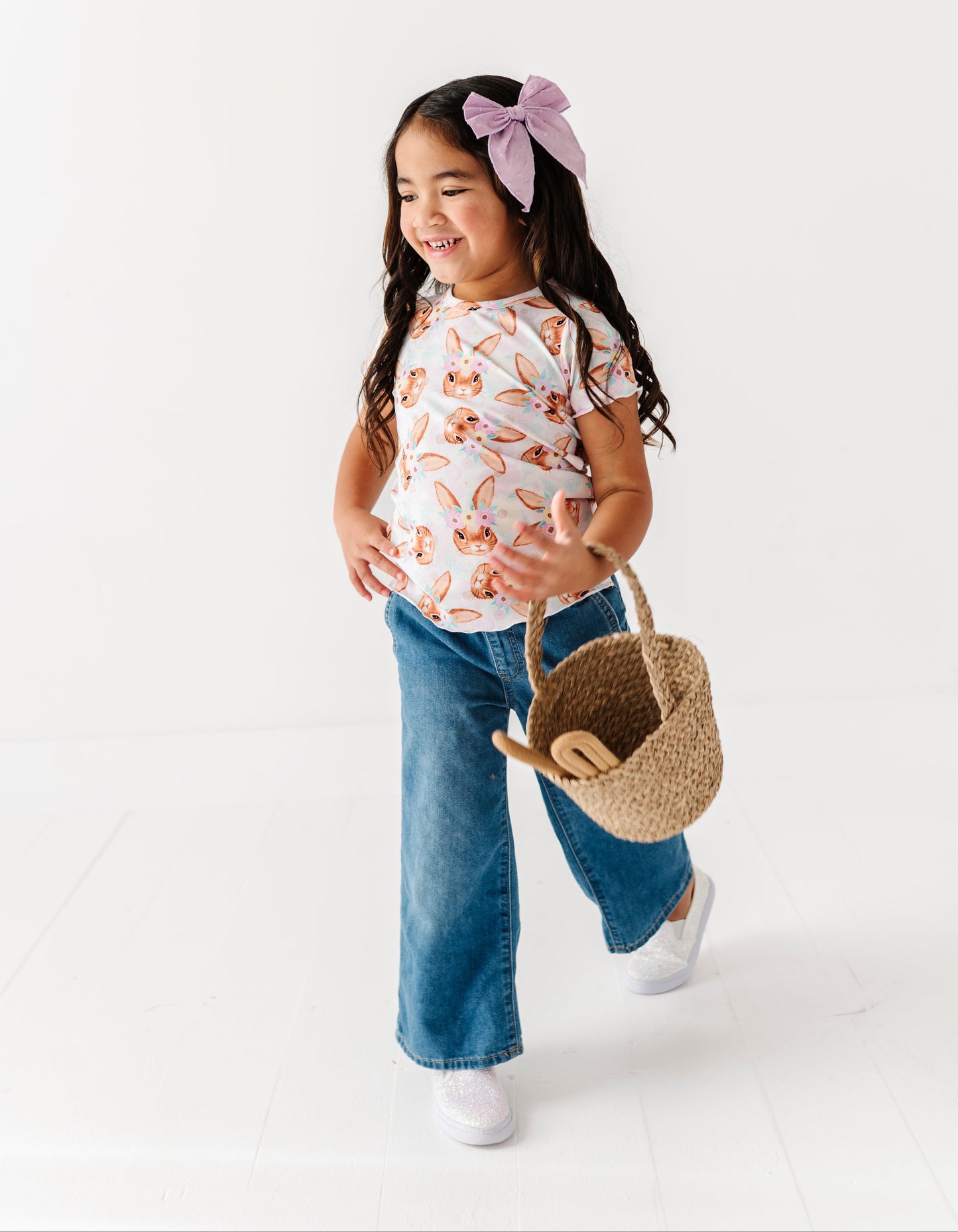 Young girl holding a straw bag, wearing a floral shirt and blue jeans, on a white background