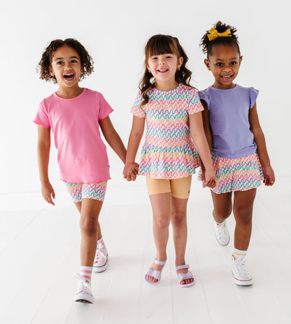 Three children holding hands and smiling, wearing colorful outfits on a white background