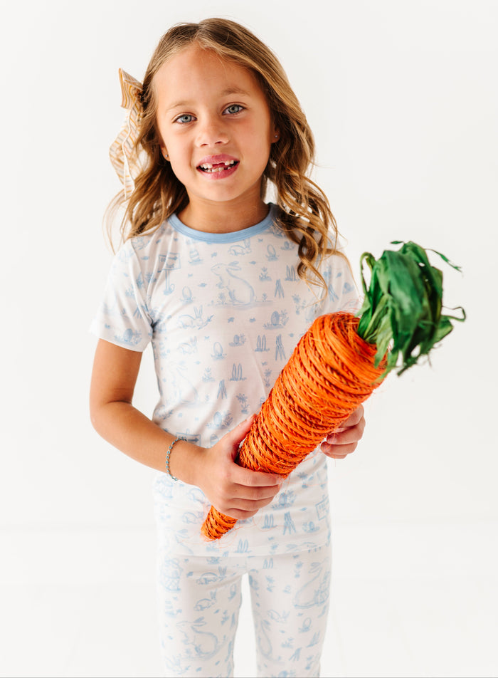 Young girl wearing a bamboo Easter pajama set holding a large carrot against a white background