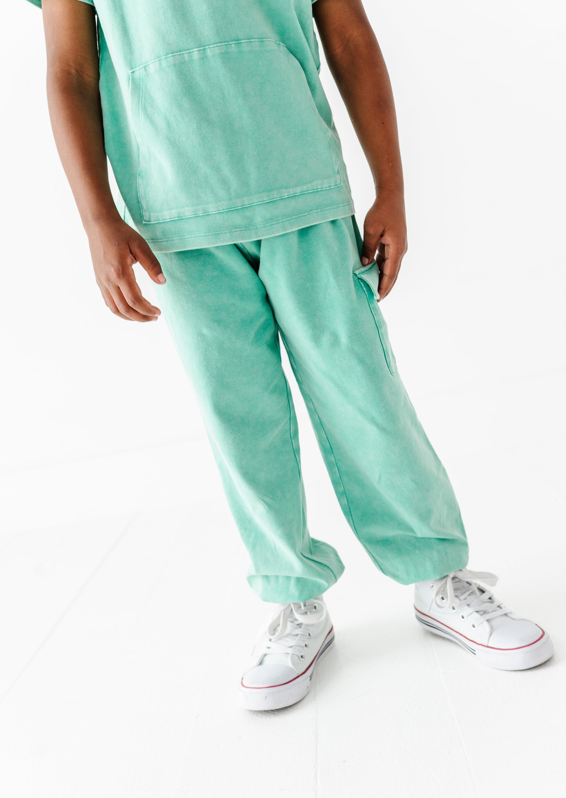 Child wearing a light green outfit with white sneakers on a white background